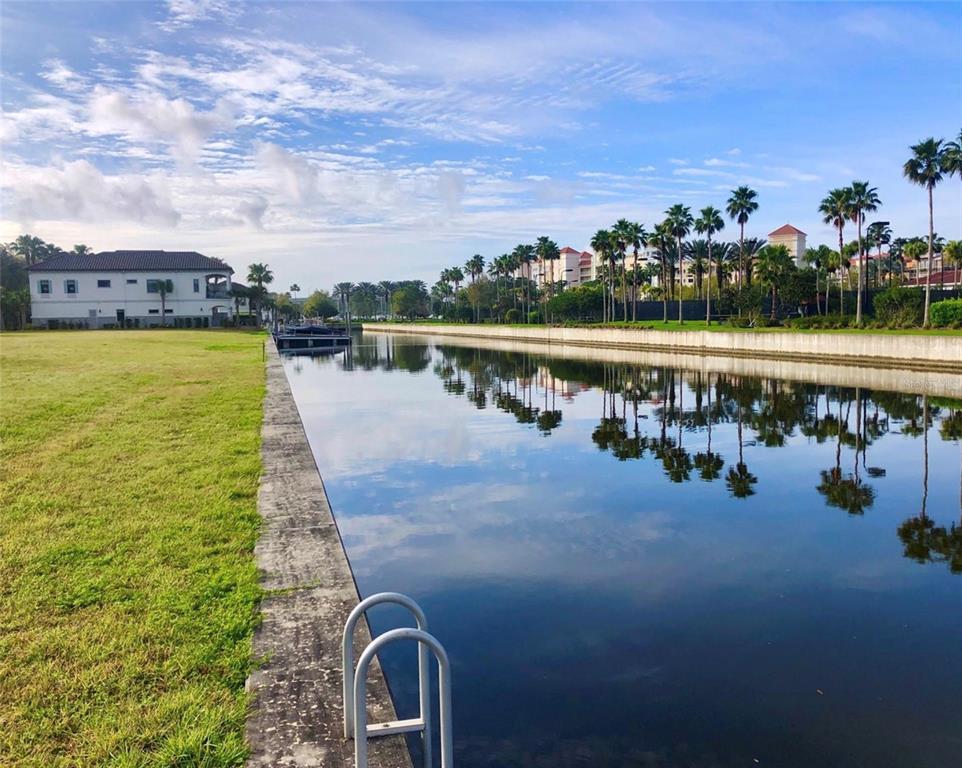 A canal view with a grassy lawn, a concrete bulkhead, and palm trees in the distance — 234 HARBOR VILLAGE POINT N, PALM COAST, FL