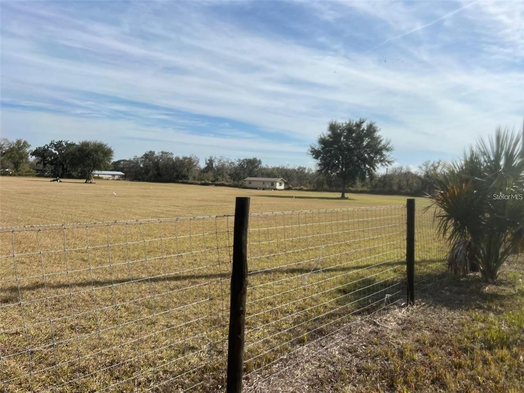 A wire fence borders a large, open grassy field with trees and a small building — HART ROAD, WAUCHULA, FL