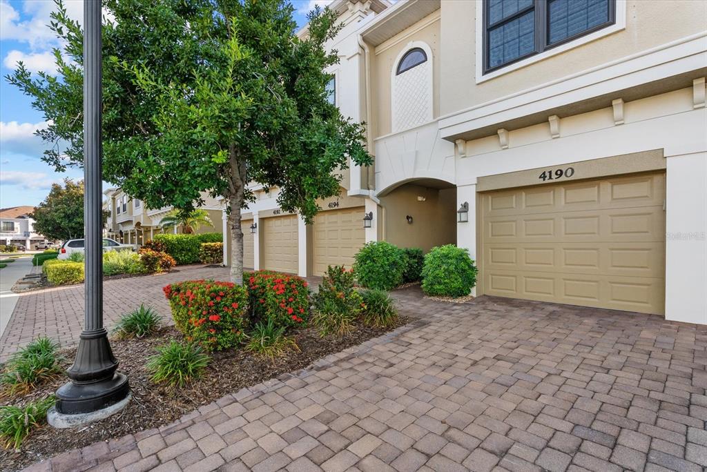 A row of townhomes with tan garages and paver driveways under a cloudy sky — 4190 OVERTURE CIRCLE UNIT 511, BRADENTON, FL