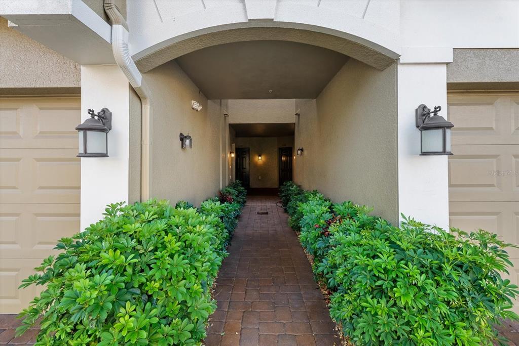 A paved walkway leads between two garage doors toward a recessed entryway with landscaping — 4190 OVERTURE CIRCLE UNIT 511, BRADENTON, FL