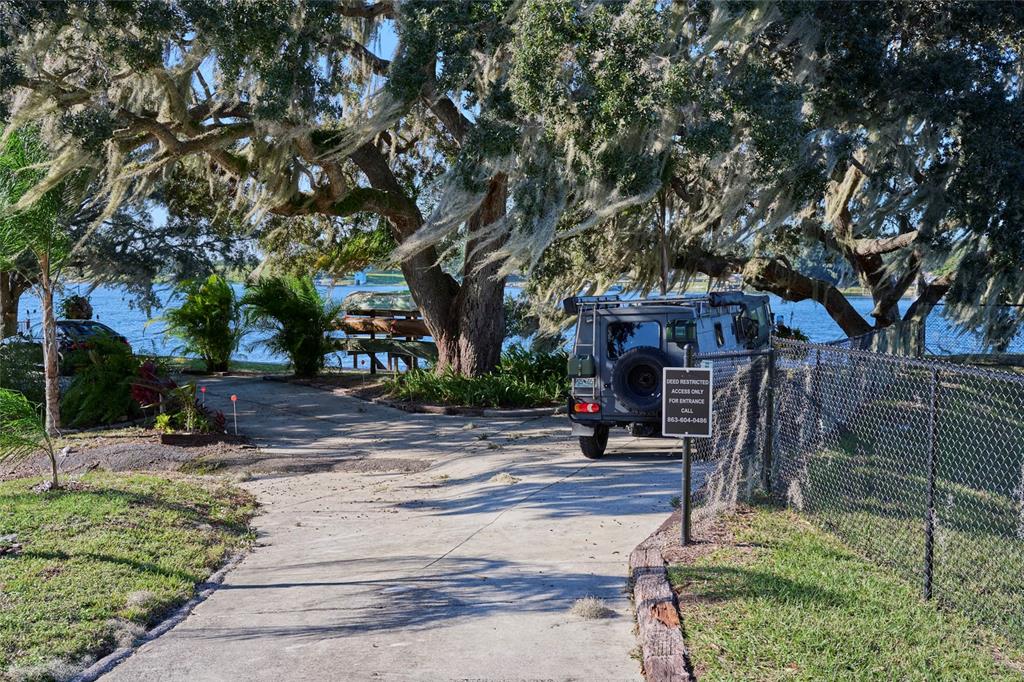 A paved driveway leads toward a lake under large oak trees with a parked vehicle — 0 SUNSET TRAIL, BABSON PARK, FL