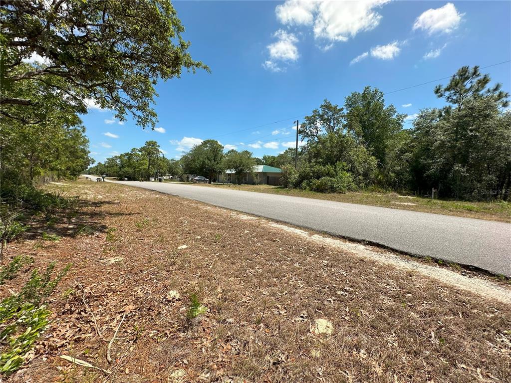 A paved road runs through a wooded area with a house visible in the distance — 671 N GRIFFITH AVENUE, CRYSTAL RIVER, FL
