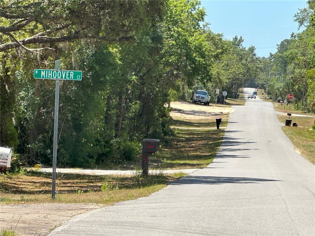 A street sign for Mihoover Court stands beside a paved road lined with trees and mailboxes — 671 N GRIFFITH AVENUE, CRYSTAL RIVER, FL