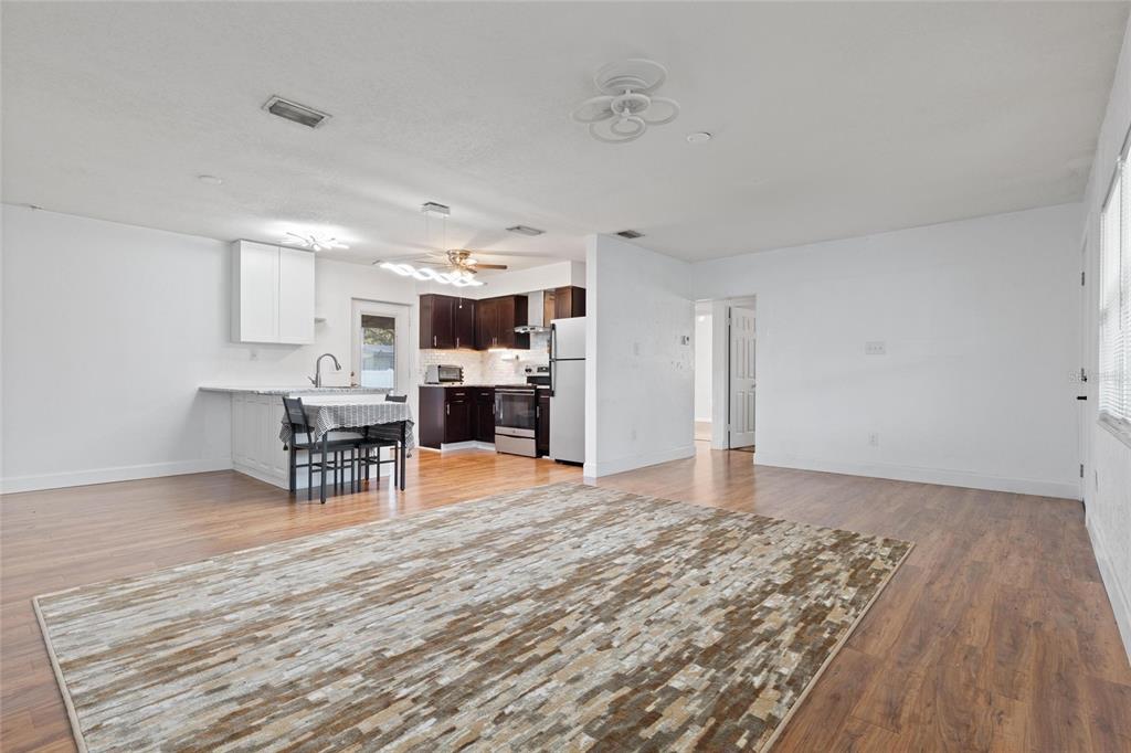 An open-concept living and dining area features wood-look flooring, white walls, and a modern kitchen — 10811 VALENCIA TERRACE, SEMINOLE, FL