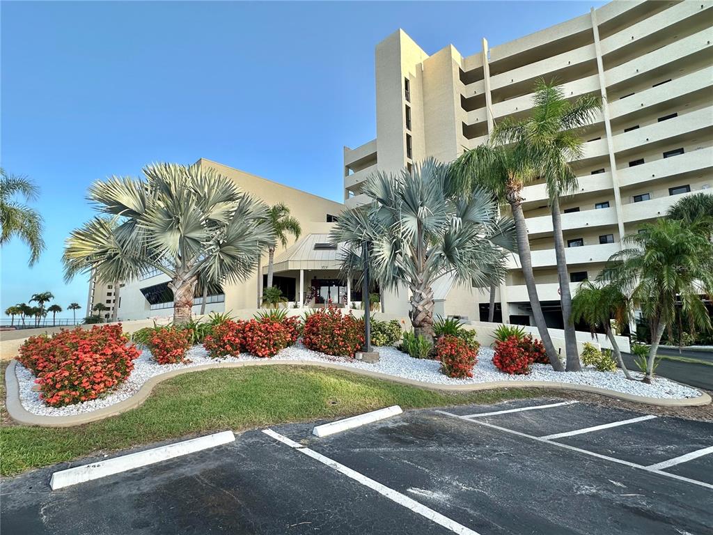 A multi-story building exterior features a parking lot, landscaped flower beds, and several palm trees — 5915 SEA RANCH DRIVE UNIT 603, HUDSON, FL