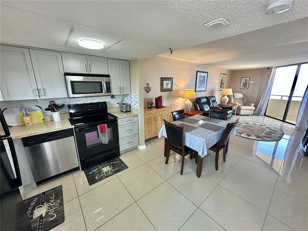 An open-concept kitchen and dining area features light cabinetry, stainless steel appliances, and tile flooring — 5915 SEA RANCH DRIVE UNIT 603, HUDSON, FL