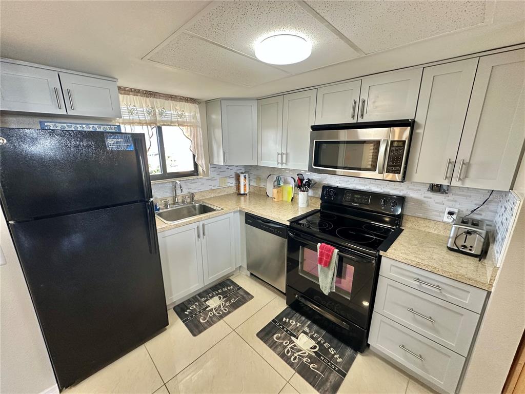 A kitchen features light gray cabinets, stainless steel appliances, a black refrigerator, and beige countertops — 5915 SEA RANCH DRIVE UNIT 603, HUDSON, FL