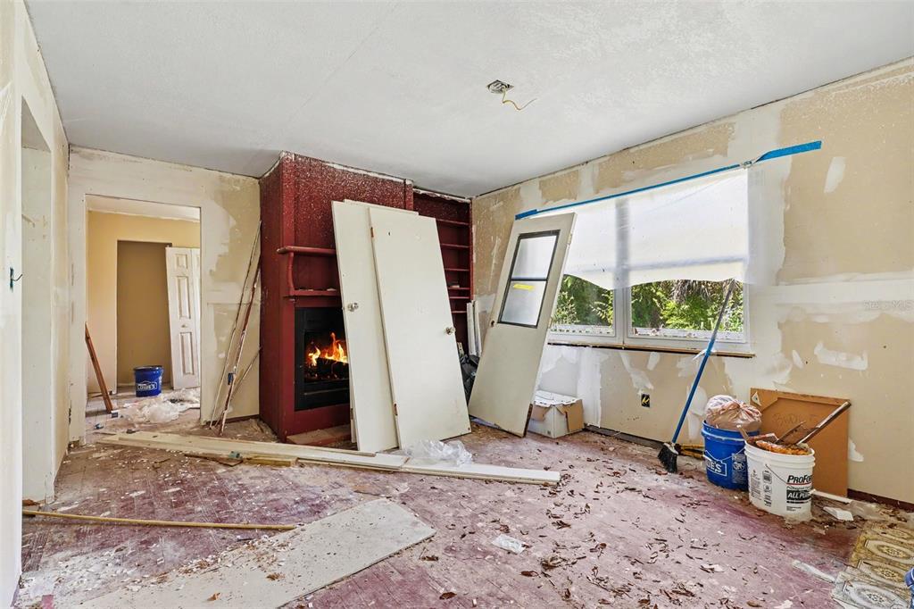 A room under renovation features a red fireplace, exposed walls, and scattered construction debris — 4195 E RAILROAD AVENUE, COCOA, FL