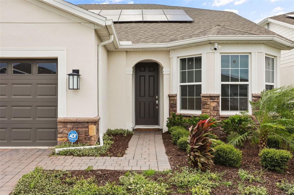 The exterior of a house features a dark front door, stone accents, and roof solar panels — 13355 SUNNY RETREAT LANE, WINTER GARDEN, FL