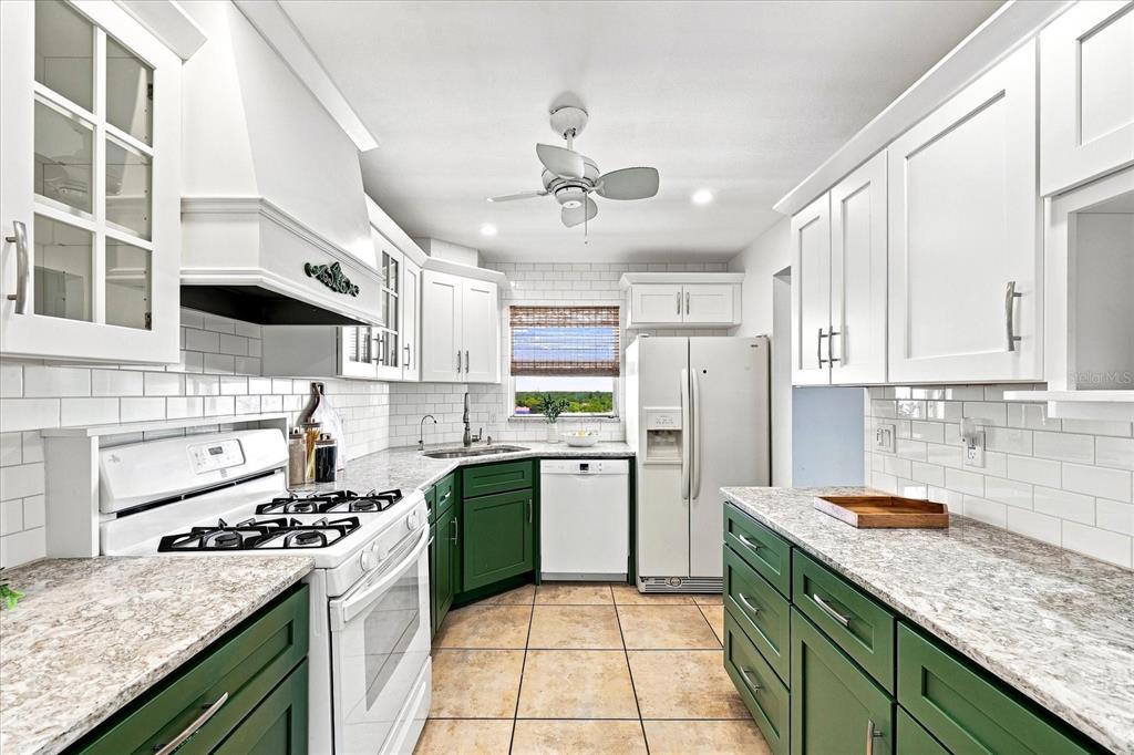 A kitchen features white upper cabinets, green lower cabinets, white appliances, and granite countertops — 6020 SHORE BOULEVARD S UNIT 1002, GULFPORT, FL