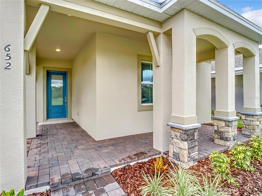 A covered front porch features a blue door, stone-based columns, and a brick paver floor — 652 KIMBER LANE, DEBARY, FL