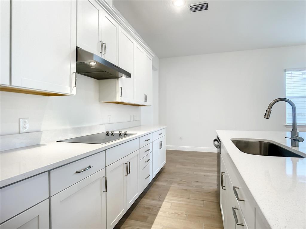 A modern kitchen features white cabinets, quartz countertops, stainless steel appliances, and wood-look tile flooring — 652 KIMBER LANE, DEBARY, FL