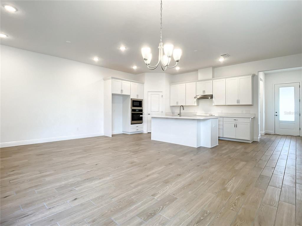 A bright, open-concept kitchen features white cabinetry, a center island, and light wood-look flooring — 652 KIMBER LANE, DEBARY, FL