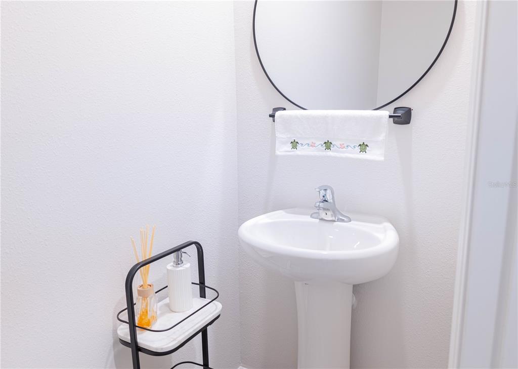 A small bathroom features a white pedestal sink, a round mirror, and a tiered shelf — 17632 CRESCENT MOON LOOP, BRADENTON, FL