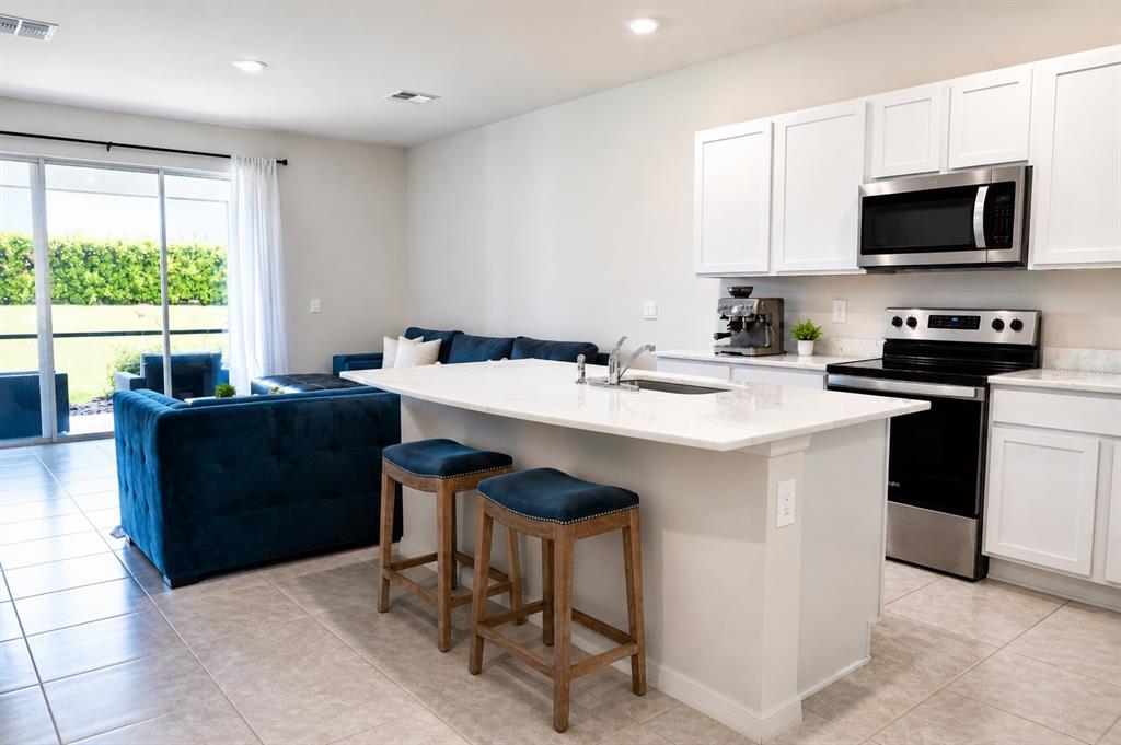 A kitchen with white cabinets and a quartz island overlooks a living area with blue furniture — 17632 CRESCENT MOON LOOP, BRADENTON, FL