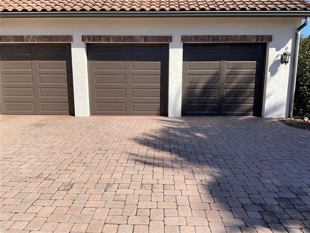 A three-car garage with brown paneled doors and a brick-paved driveway — 11406 WATERSTONE LOOP DRIVE, WINDERMERE, FL