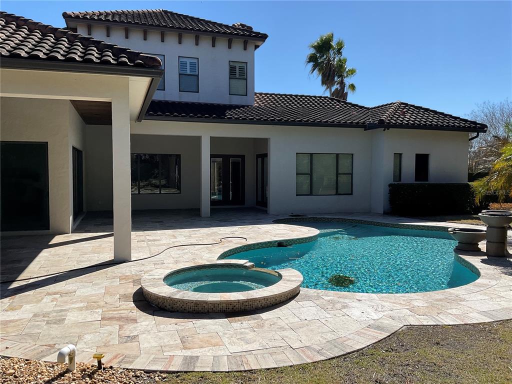 A backyard features a swimming pool, a raised spa, and a covered patio with stone pavers — 11406 WATERSTONE LOOP DRIVE, WINDERMERE, FL