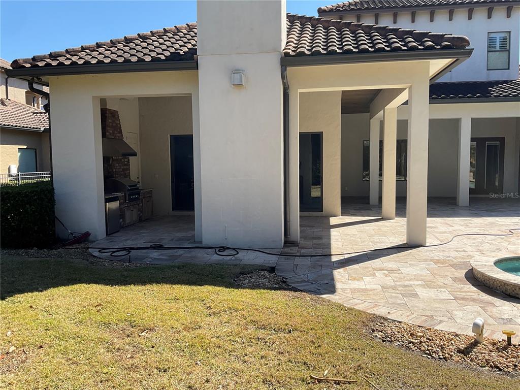 A covered outdoor kitchen and patio area with stone flooring and a pool edge — 11406 WATERSTONE LOOP DRIVE, WINDERMERE, FL