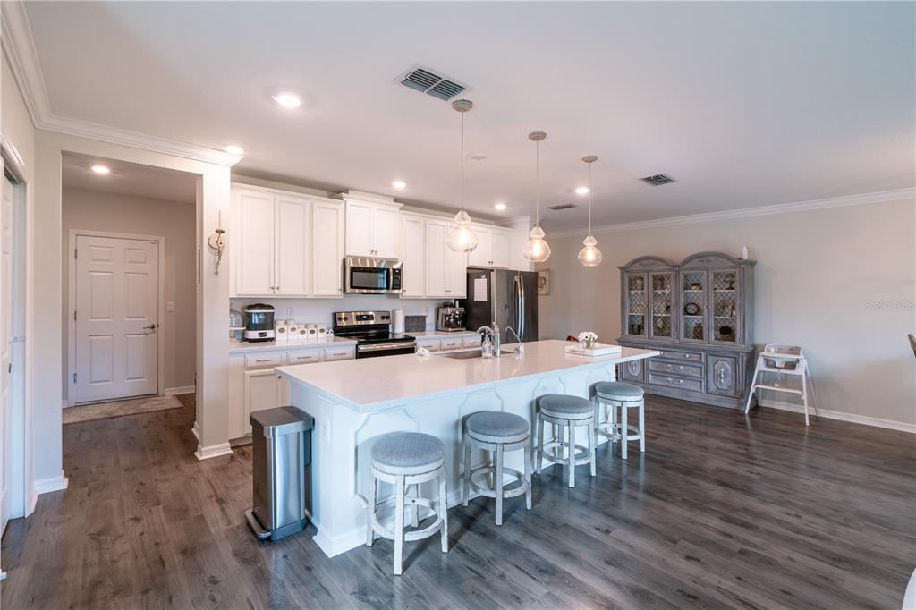 A kitchen features a large white island with bar stools, white cabinetry, and wood flooring — 16261 YELLOWEYED DRIVE, CLERMONT, FL