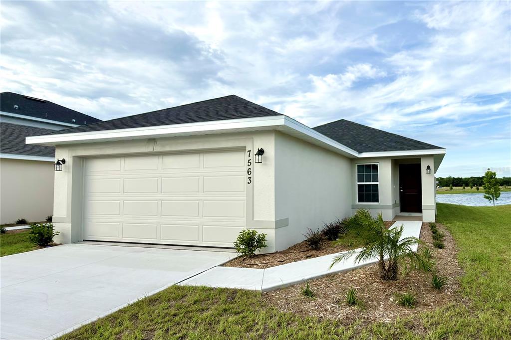 A single-story house with a two-car garage, light stucco exterior, and a dark shingled roof — 7563 BENT TREE LOOP, ST CLOUD, FL