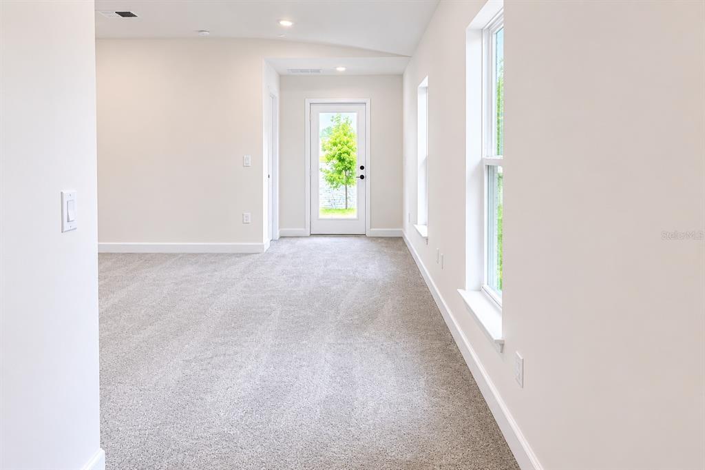 An empty room with gray carpet, white walls, two windows, and a glass-paneled exterior door — 7563 BENT TREE LOOP, ST CLOUD, FL