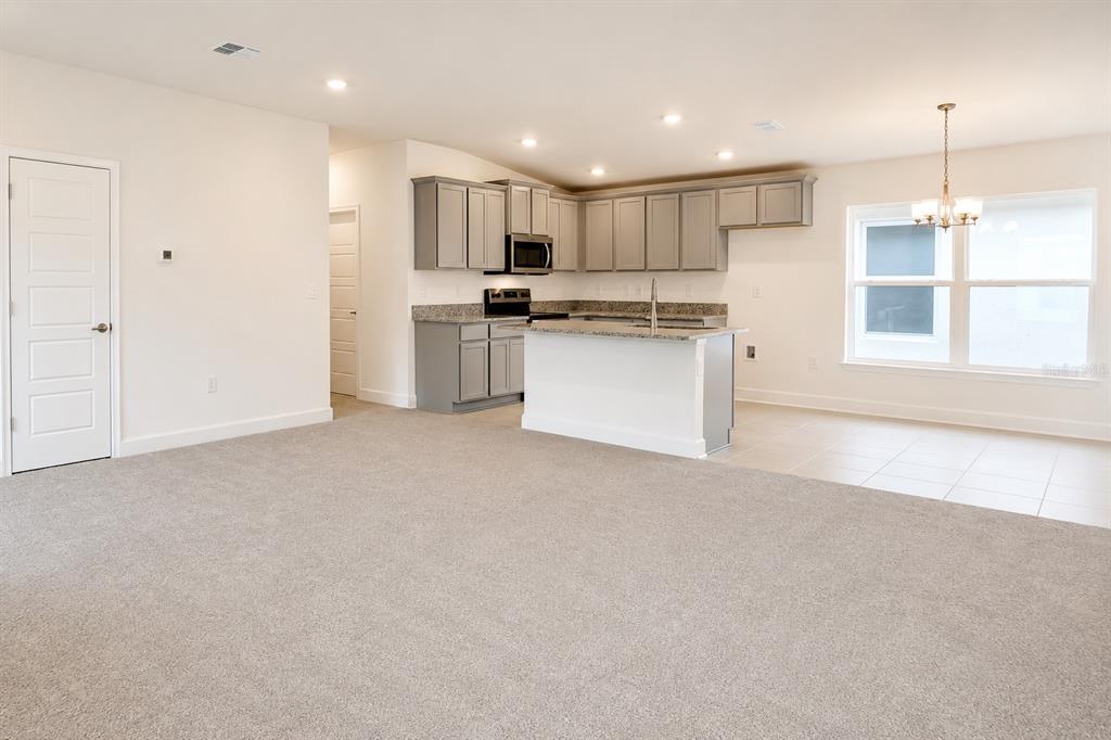 An open-concept kitchen with gray cabinets and a central island overlooks a carpeted living area — 7563 BENT TREE LOOP, ST CLOUD, FL