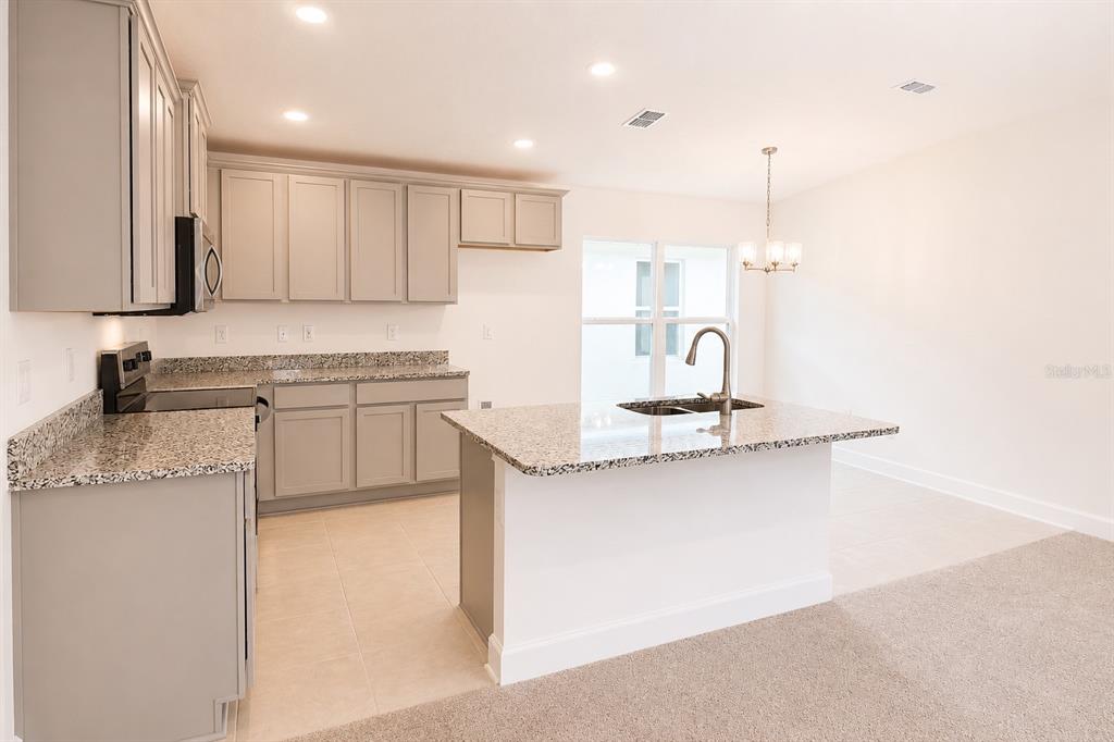 A kitchen with gray cabinets, granite countertops, a center island, and light-colored tile flooring — 7563 BENT TREE LOOP, ST CLOUD, FL
