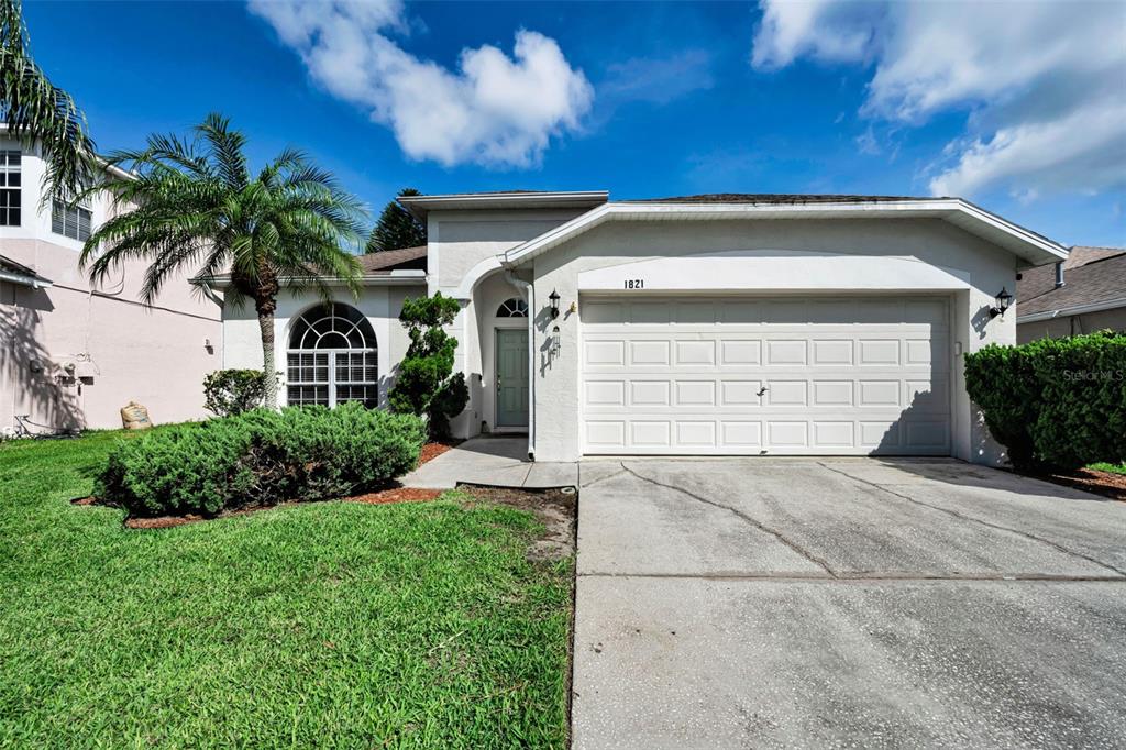 A single-story house with a white stucco exterior, a two-car garage, and a palm tree — 1821 ALVARA PLACE, TRINITY, FL