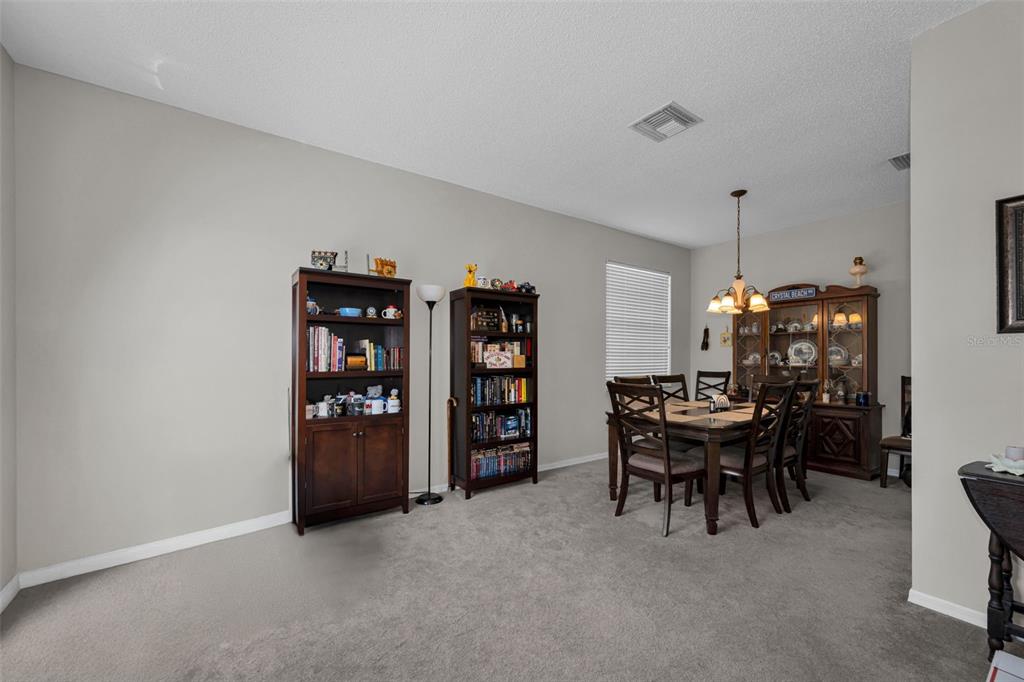 A dining room features carpeted flooring, two bookshelves, and a wooden dining set — 1821 ALVARA PLACE, TRINITY, FL
