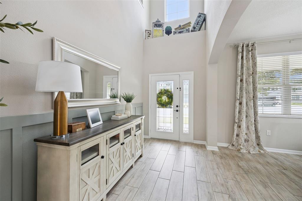 A bright entryway features a wood-topped console table, wainscoting, and a high ceiling with windows — 162 BLUE FLAX POINT, LONGWOOD, FL