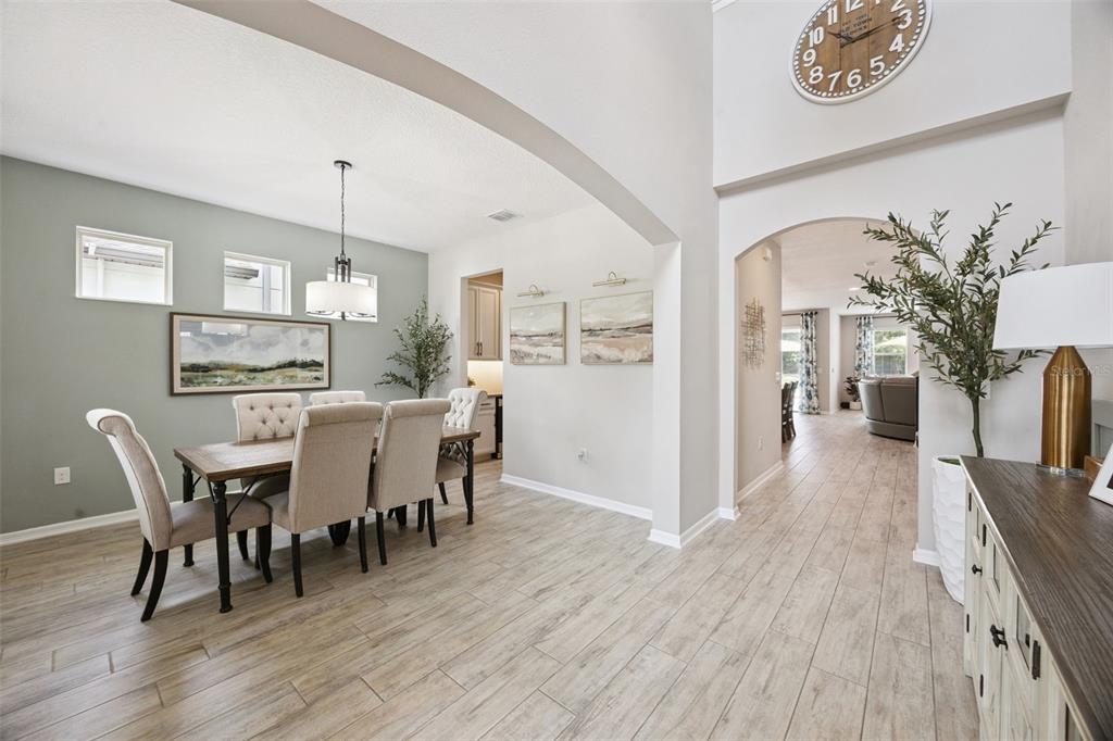 A dining room with light wood floors, a large wall clock, and an arched entryway — 162 BLUE FLAX POINT, LONGWOOD, FL