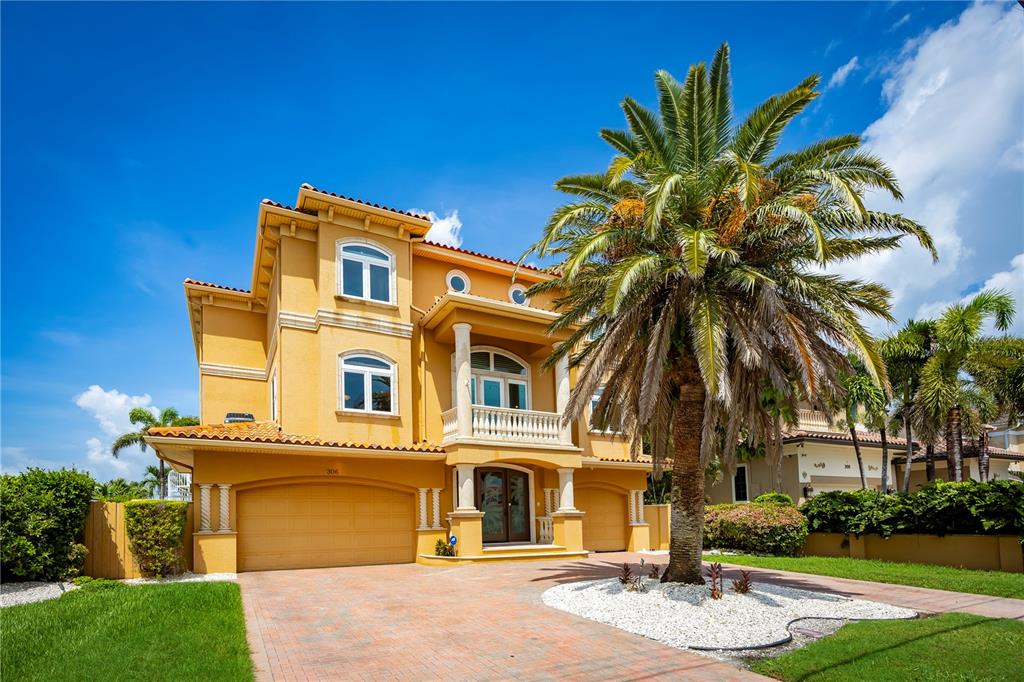 A three-story yellow stucco house with a palm tree and a paved driveway — 306 HARBOR DRIVE, INDIAN ROCKS BEACH, FL