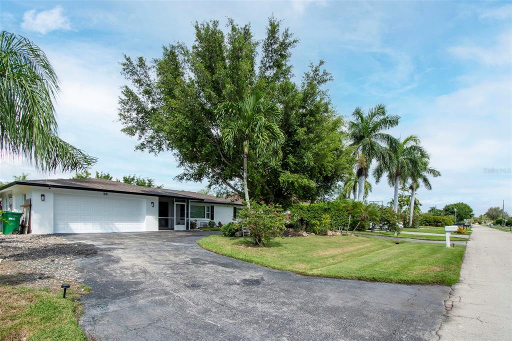 A single-story house with a white garage, a paved driveway, and several tall palm trees — 59 WICKLIFFE DRIVE, NAPLES, FL