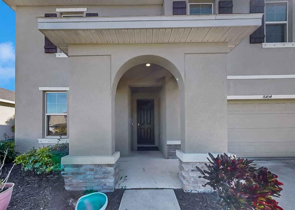 A two-story house exterior features a covered arched entryway, stone accents, and a garage — 16454 WOODSIDE GLEN, PARRISH, FL