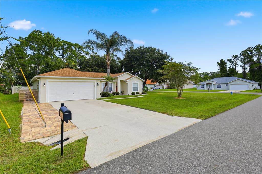 A single-story suburban house with a two-car garage, concrete driveway, and a palm tree — 23 PORT LANE, PALM COAST, FL