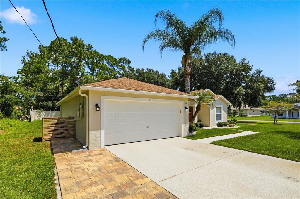 A single-story house with a white garage door, a paved driveway, and a palm tree — 23 PORT LANE, PALM COAST, FL