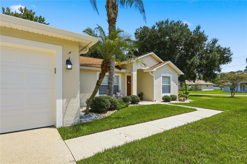 A single-story house with a beige stucco exterior, a palm tree, and a concrete walkway — 23 PORT LANE, PALM COAST, FL