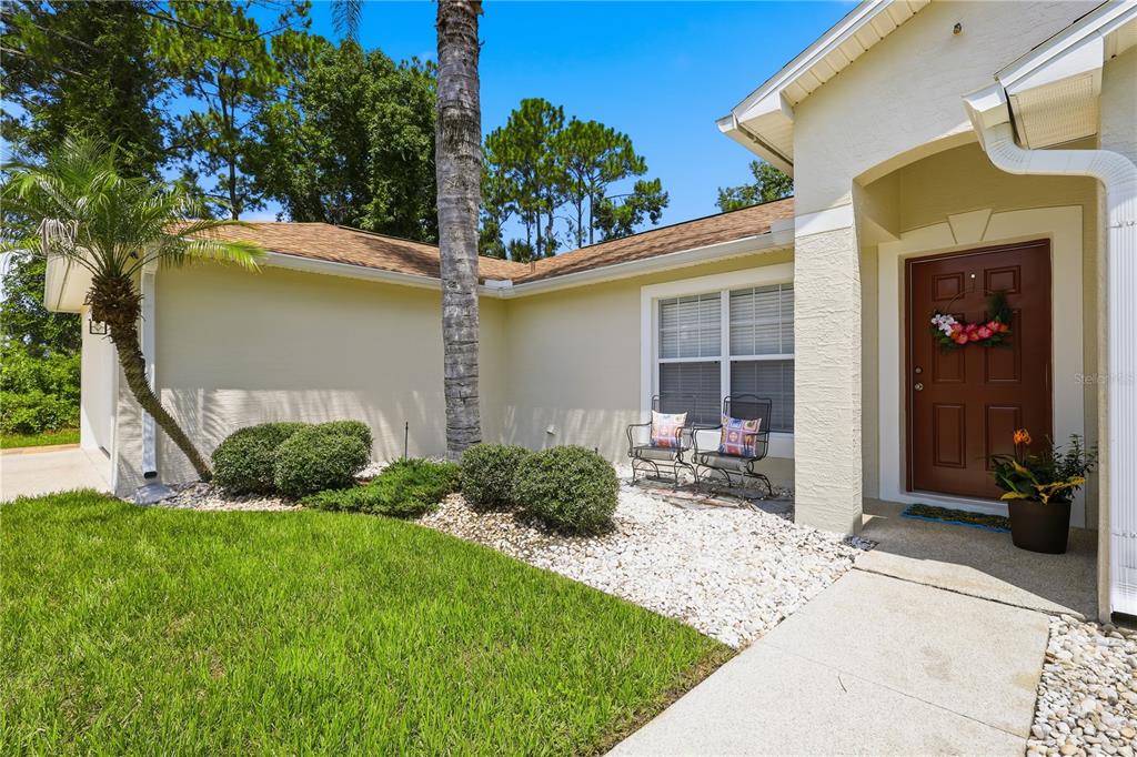 A tan house exterior features a brown front door, a palm tree, and a stone garden — 23 PORT LANE, PALM COAST, FL