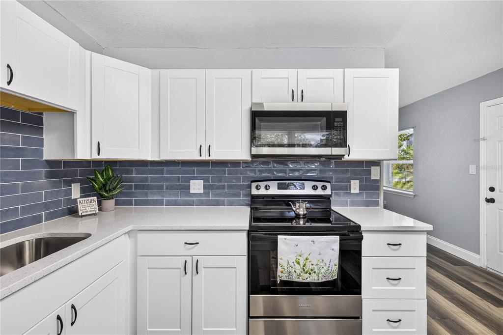 A kitchen features white cabinets, a blue subway tile backsplash, and stainless steel appliances — 1803 E OHIO STREET, PLANT CITY, FL