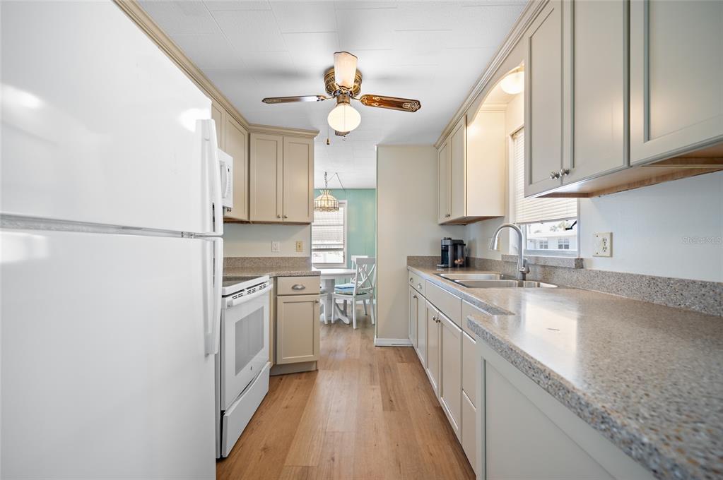 A galley kitchen features light-colored cabinets, speckled countertops, white appliances, and wood-look flooring — 5751 HYACINTH ROAD, VENICE, FL