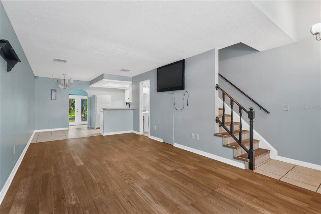 An open living room with wood-look flooring, a staircase, and a view into the kitchen — 609 SAINT HENRY DRIVE, BRANDON, FL