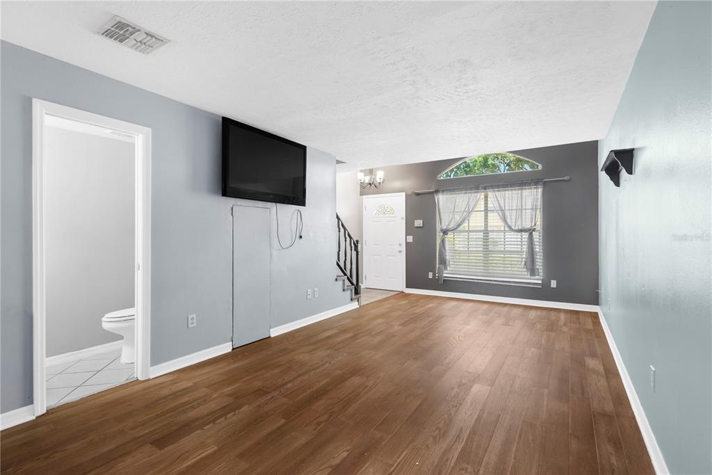 A living room with wood-look flooring, a wall-mounted television, and a view of an entryway — 609 SAINT HENRY DRIVE, BRANDON, FL