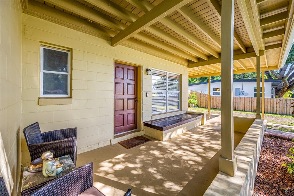 A covered concrete porch features a red front door, a built-in bench, and wicker furniture — 6410 WALTON WAY, TAMPA, FL