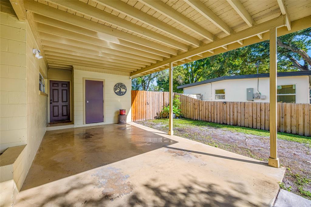 A covered concrete patio features a purple door, a wooden fence, and a tree decal — 6410 WALTON WAY, TAMPA, FL