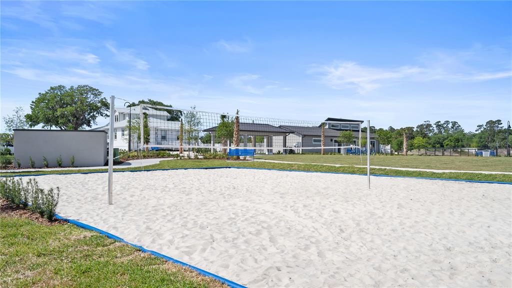 A sand volleyball court sits in front of a community building and a white house — 5566 RONIN DRIVE, ST CLOUD, FL