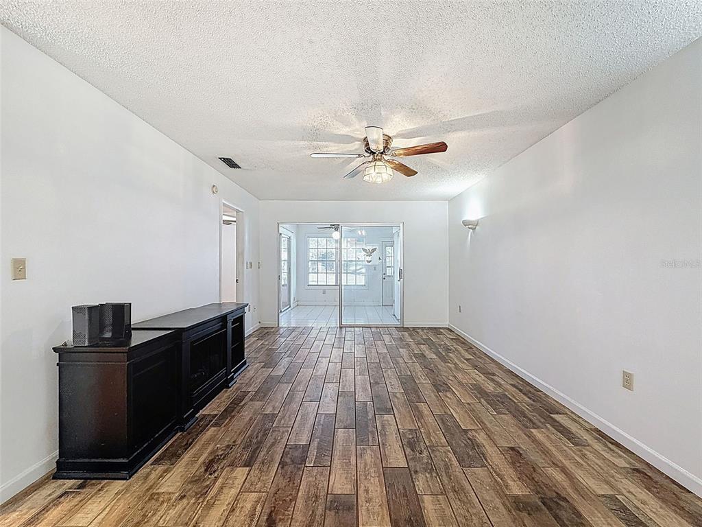 A living room features wood-look tile flooring, a ceiling fan, and a sliding glass door — 11403 VERSAILLES LANE UNIT E, PORT RICHEY, FL