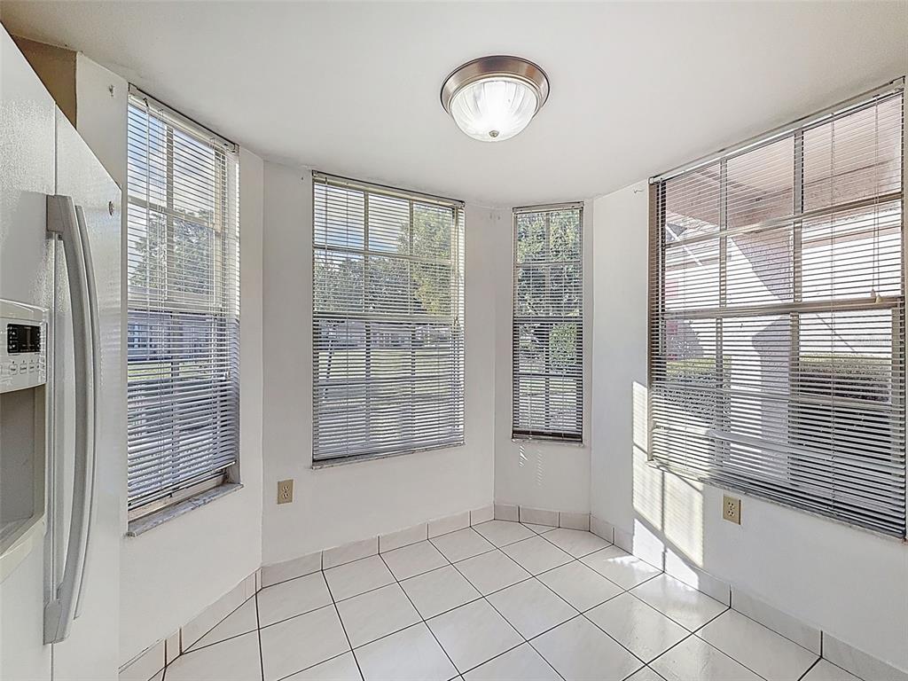 A bright breakfast nook with white tile floors, multiple windows with blinds, and a ceiling light — 11403 VERSAILLES LANE UNIT E, PORT RICHEY, FL