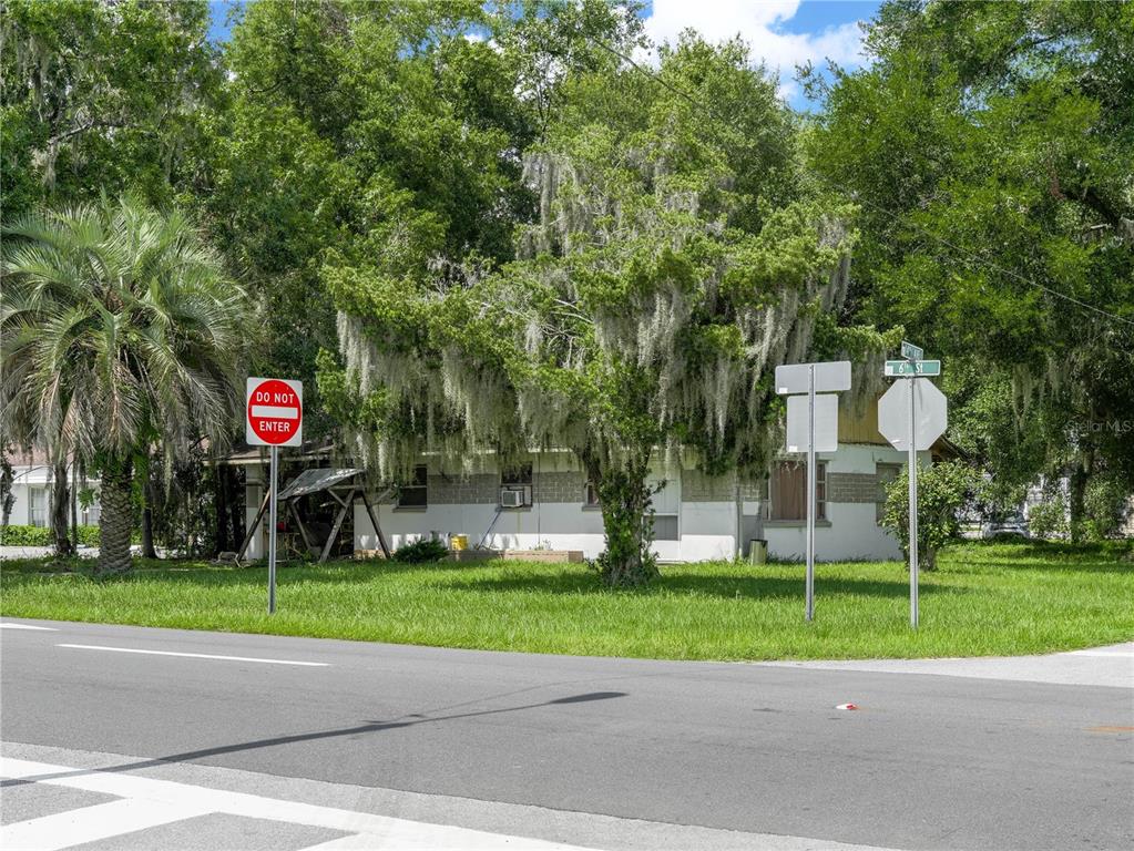 A single-story house with a white exterior sits behind a lawn and large trees — 5821 GALL BOULEVARD, ZEPHYRHILLS, FL