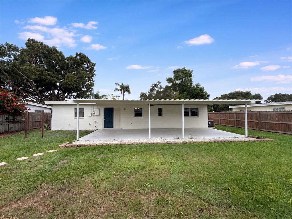 The exterior of a white house features a large covered concrete patio and wooden fencing — 1371 JEFFORDS STREET, CLEARWATER, FL