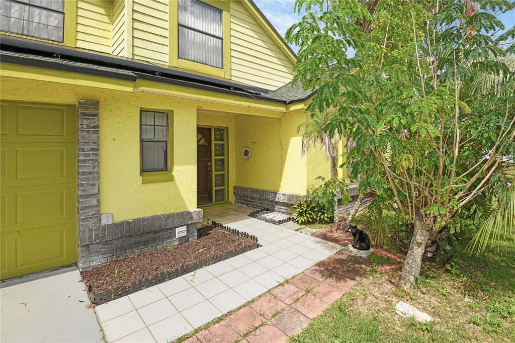 A yellow house exterior features a tiled walkway, a front door, and a black cat — 1469 MONA DRIVE, KISSIMMEE, FL